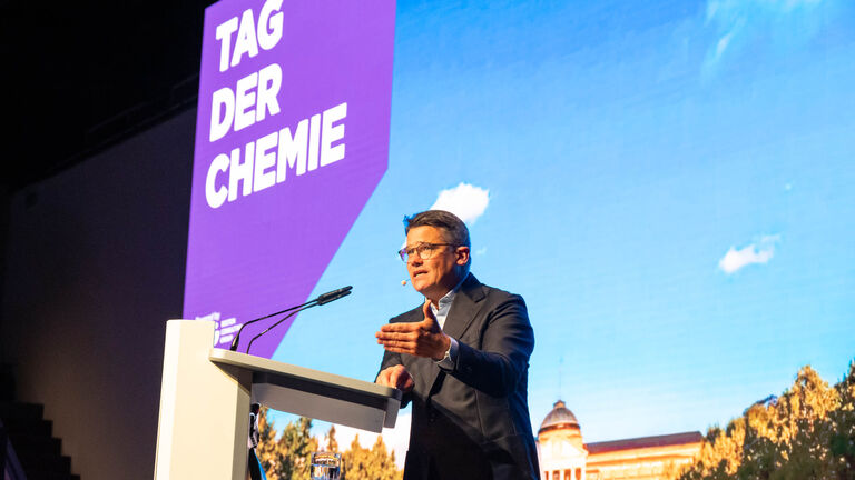Ministerpräsident Rhein spricht zum „Tag der Chemie“. Er ist zu sehen während seiner Rede, an einem Rednerpult stehend; hinter ihm eine Wand, darauf zu lesen „TAG DER CHEMIE“.