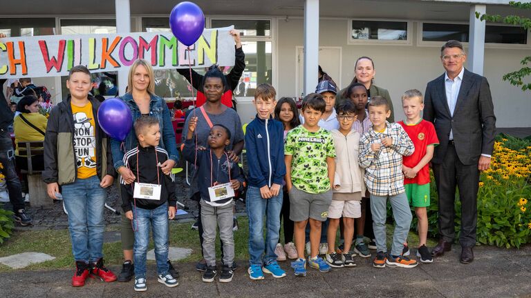 Ministerpräsident Rhein steht mit Kindern und Erwachsenen vor einem Schulgebäude zum Gruppenfoto.