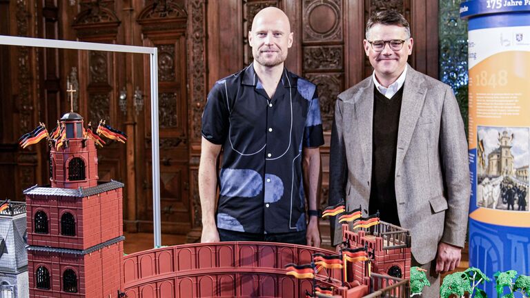 Ministerpräsident Boris Rhein eröffnet die PLAYMOBIL-Ausstellung „175 Jahre Paulskirche“ in Schloss Philippsruhe. Gemeinsam mit dem PLAYMOBIL-Künstler Oliver Schaffer steht er vor dem Diorama der Paulskirche.