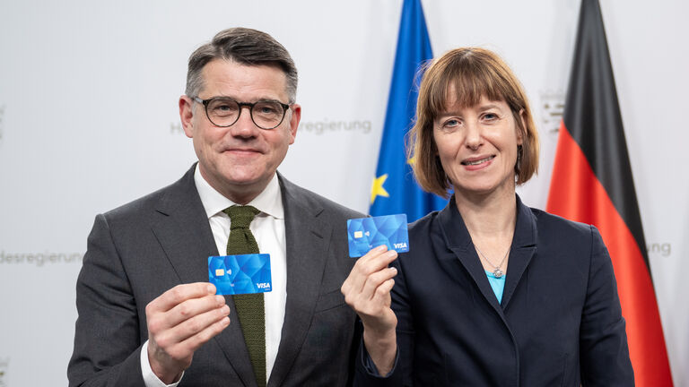 Ministerpräsident Boris Rhein und Sozialministerin Heike Hofmann stehen nebeneinander und halten jeweils eine blaue Geldkarte hoch.