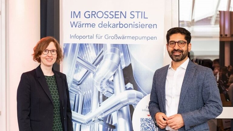 Zwei Personen stehen vor einem Banner 