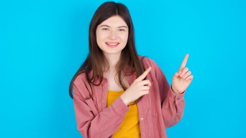 Schau mal da rüber! Mädchen steht lachend vor blauer Wand und zeigt lustig nach rechts