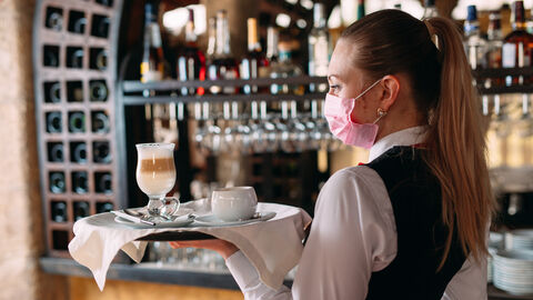Kellnerin mit Maske trägt Tablett