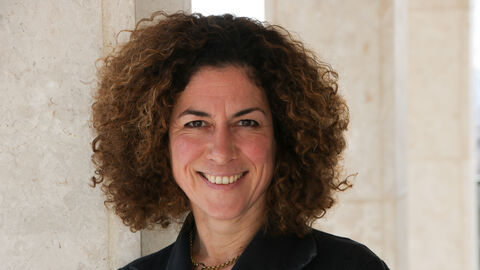 Alice Engel Alice Engel lächelt in die Kamera. Sie ist bis zur Brust zu sehen, trägt eine goldene Kette und eine schwarze Bluse.