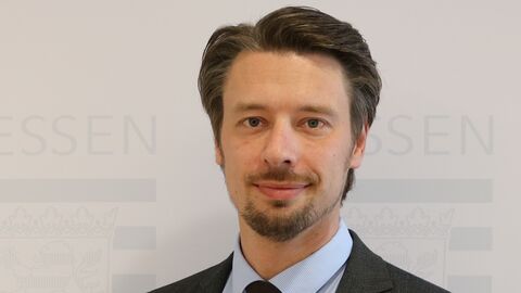 Michael Schaich Michael Schaich lächelt in die Kamera. Er trägt ein anthrazitfarbenes Sakko und eine ebensolche Krawatte, dazu ein hellblaues Hemd.