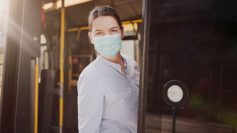 Eine Frau mit Maske steht in der Tür eines Busses. Eine Frau mit Maske steht in der Tür eines Busses.