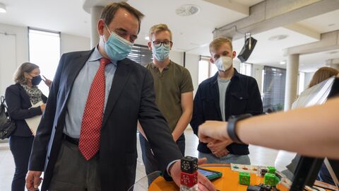 Kultusminister Lorz steht an einem Tisch, hält die Hände neben einen Würfelblock.