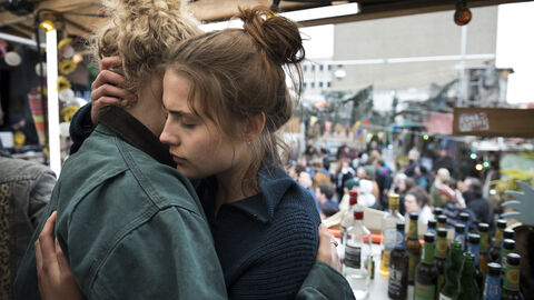 Filmszene aus "Und morgen die ganze Welt" Zwei Frauen umarmen sich. Im Hintergrund sieht man Flaschen und mehrere Menschen