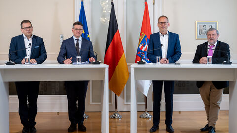 Pressekonferenz Versorgungsgipfel Dr. Christian Höftberger, Ministerpräsident Boris Rhein, Gesundheitsminister Kai Klose und Frank Dastych stehen vor drei Fahnen und halten eine Pressekonferenz ab. Sie stehen an Stehtischen und haben Mikrofone vor sich.