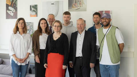 Justizstaatssekretärin Eichner mit Auszubildenden und weiteren Beteiligten vor einer weißen Wand in einem Raum des Unternehmens.