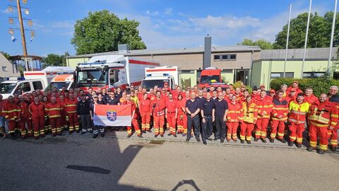 Gruppenbild der hessischen Einsatzkräfte vor einem Gebäude mit Einsatzfahrzeugen.