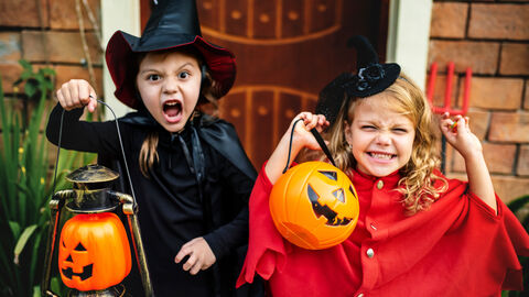 Süßes oder Saures! Zwei Kinder in Halloweenkostümen machen Gruselposen und lachen.