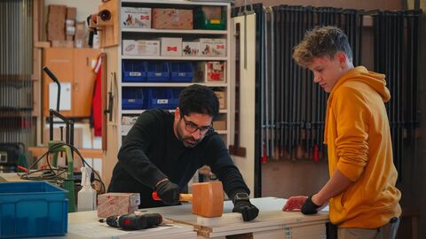 Wirtschaftsminister Mansoori in Werkstatt Wirtschaftsminister Mansoori steht in einer Werkstatt über einen Tisch gebeugt mit einem Hammer. Neben ihm steht ein junger Mann, der seine Tätigkeit beobachtet.