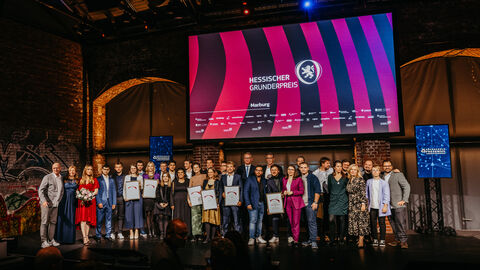 Verleihung Hessischer Gründerpreis 2024 Mehrere Menschen stehen auf Bühne. Auf dem Monitor im Hintergrund steht "Hessischer Gründerpreis"