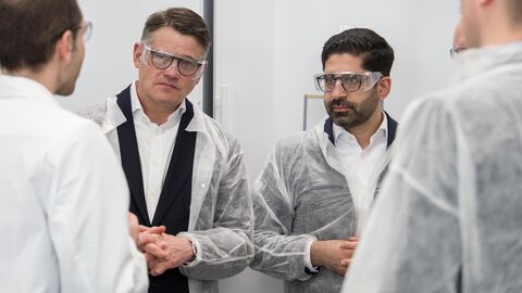 Ministerpräsident Boris Rhein (links) und der stellvertretende Regierungschef, Wirtschaftsminister Kaweh Mansoori (rechts), beim Biotechnologie-Unternehmen BioSpring, beide tragen Schutzbrille und -kittel.