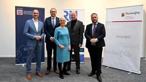 Vier Männer und eine Frau lachen in die Kamera. Hinter Ihnen stehen Plakate mit den beiden Logos vom hessischen und rheinland-pfälzischen Wissenschaftsministerium.