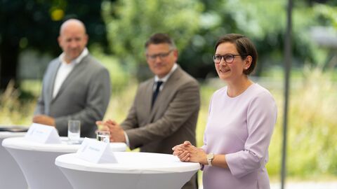 Zwei Männer und eine Frau stehen an Pult.