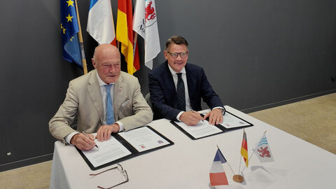 Ministerpräsident Boris Rhein und Alain Rousset, Präsident des Regionalrats der Nouvelle-Aquitaine, bei der Unterzeichnung des MoU Zwei Männer sitzen nebeneinander an einem Tisch und sind gerade dabei ein Dokument zu unterzeichnen.