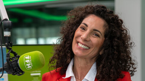 Eine Frau lächelt in die Kamera. Neben ihr hängt ein Mikrofon.