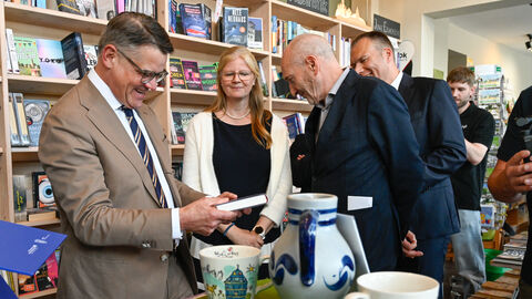 Ministerpräsident Boris Rhein steht in einer Buchhandlung und schaut sich ein Buch an - um ihn herum mehrere Personen.