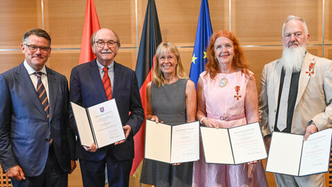 Der Ministerpräsident steht neben zwei Männern und zwei Frauen - alle vier zeigen Urkunden in die Kamera. 