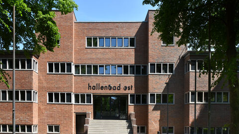 Der erste Preis beim Hessischen Denkmalschutzpreis 2022 in der Kategorie "Transformatives Bauen"  ehrte Marc Köhler, Thomas Meyer und Keivan Karampour von Karampour + Meyer Architekten PartmbB. Sie haben das ehemalige Hallenbad Ost in Kassel zu einem Ort für Veranstaltungen, Büros und Praxen umgestaltet. Das ehemalige Hallenbad Kassel Ost von außen: Ein rot gehaltener Backsteinbau