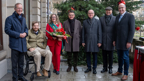 Waldbesitzer überreichen Weihnachtsbaum für die Hessische Staatskanzlei Ministerpräsident Rhein und Staatsminister Wintermeyer mit der Hessischen Weihnachtsbaumkönigin Alexa von Lewinski, dem Vizepräsident des Waldbesitzerverbandes, Roland Seel, dem geschäftsführenden Direktor des Waldbesitzerverbands, Christian Raupach, und Mitglied des Präsidiums und Vertreter für den Gemeinschaftswald, Frank Wiegand. Alle stehe nebeneinander vor dem Weihnachtsbaum.