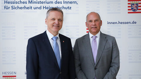 Staatssekretär Rößler steht neben Innenminister Poseck vor einer Austellwand des Ministeriums des Innern, für Sicherheit und Heimatschutz