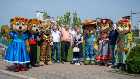 Ministerpräsident Rhein mit seiner Frau und weiteren Personen und Maskottchen stehen nebeneinander und winken.