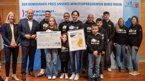 2. Preis: Kampfsportverein-Kirchvers e.V. – Die Vereinszukunft im Blick „go to Kids – ready for next step” Eine Gruppe Personen steht vor einem Aufsteller mit der Aufschrift "Der Demografie-Preis unseres Ministerpräsidenten Boris Rhein". Eine Person hält eine gerahmte Urkunde in Händen, eine weitere einen Scheck.