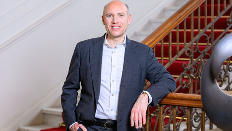 Ein Mann im blauen Anzug lehnt an einem Treppengeländer