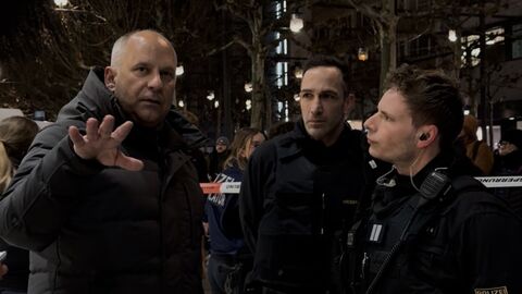 Innenminister Poseck und zwei Polizeibeamte stehen nachts auf einem Gehweg und unterhalten sich. 