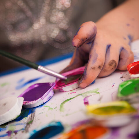 Ran an die Farben! Hand eines Kindes mit Wasserfarbe verschmiert und Pinsel in der Hand an einem Farbkasten