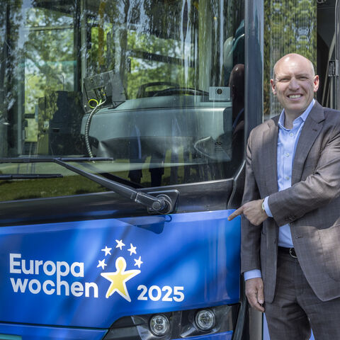 Der hessische Europaminister mit einem Europabus aus Hessen. Manfred Pentz zeigt lachend auf einen blauen Europabus